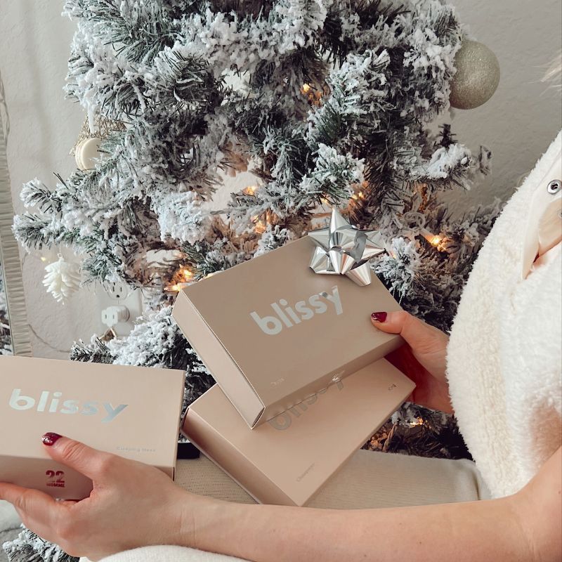 Blissy gift boxes held beside a snowy Christmas tree for a meaningful holiday gift