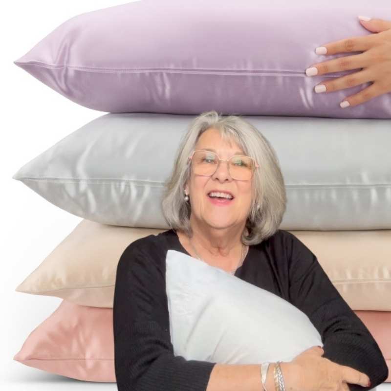 Smiling woman holding a silk pillow while stacked silk pillowcases show smooth fabric that protects skin and hair
