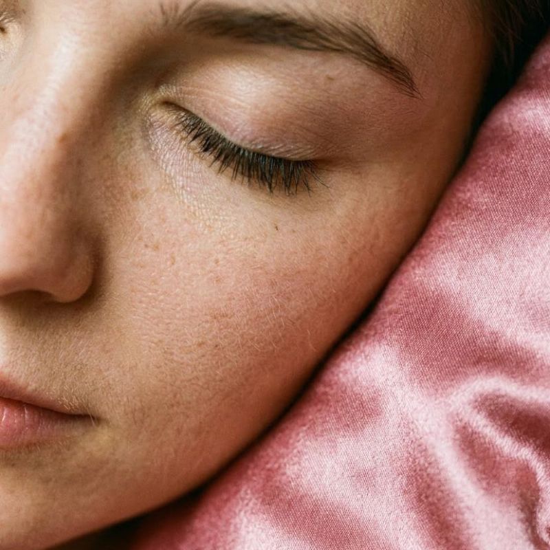 Person sleeping on a pink satin pillowcase, highlighting satin’s effects on skin and hair